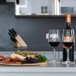 Deux verres de vin rouge sur un comptoir de cuisine moderne en marbre gris à côté d'un plateau de fromage et de charcuterie.